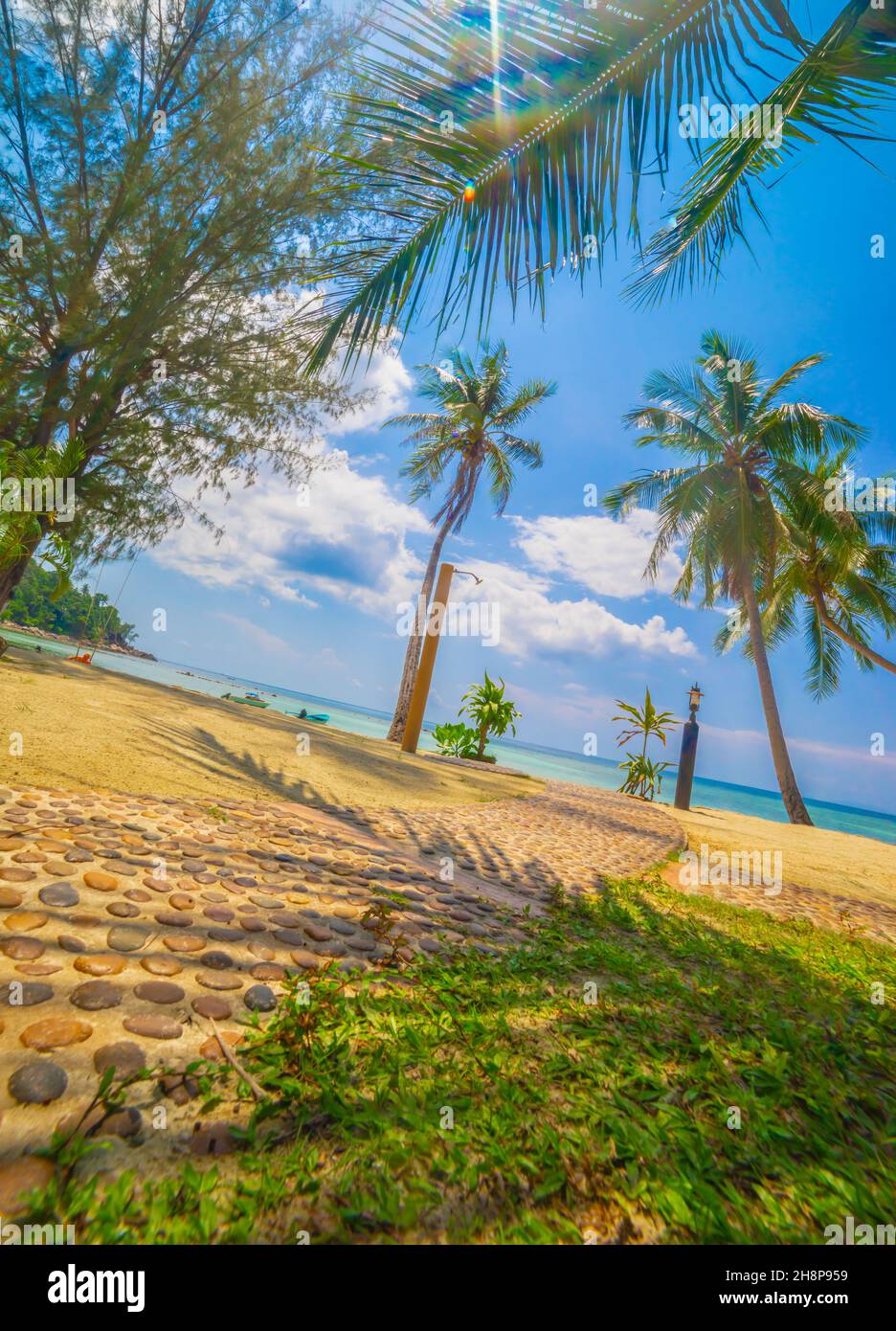 Landschaftsansicht auf leerem Strand mit Dusche mit frischem Wasser vor dem welligen Meer und dramatischen bewölkten Himmel bei Sonnenaufgang mit Palmen. Kleiner Pfad Stockfoto