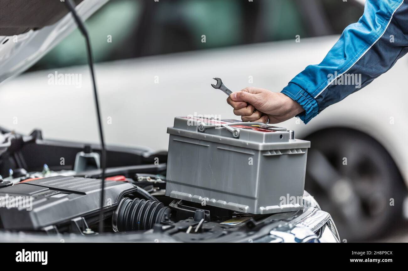 Mechaniker hält Schlüssel über der Autobatterie mit geöffnetem Motorraum des Autos. Stockfoto
