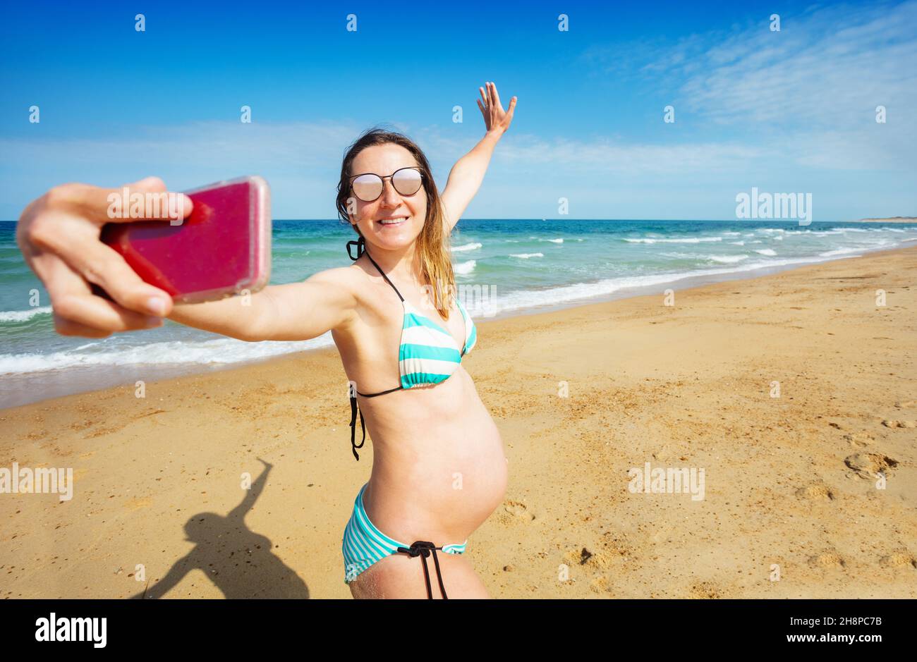 Eine Schwangerin am Strand macht Selfie mit dem Telefon Stockfoto