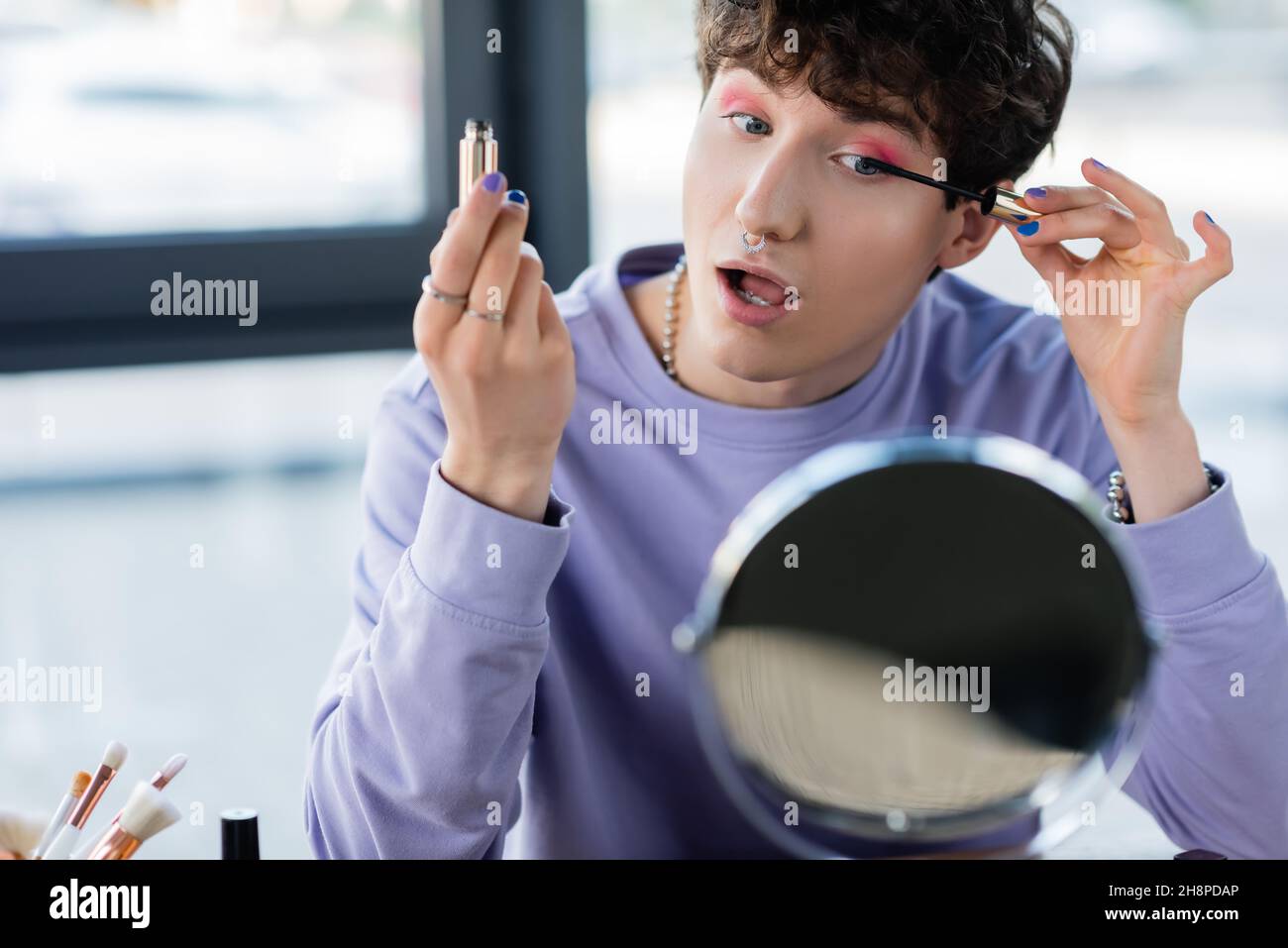 Transgender Person Anwendung Mascara in der Nähe von kosmetischen Bürsten und Spiegel, Stock Bild Stockfoto