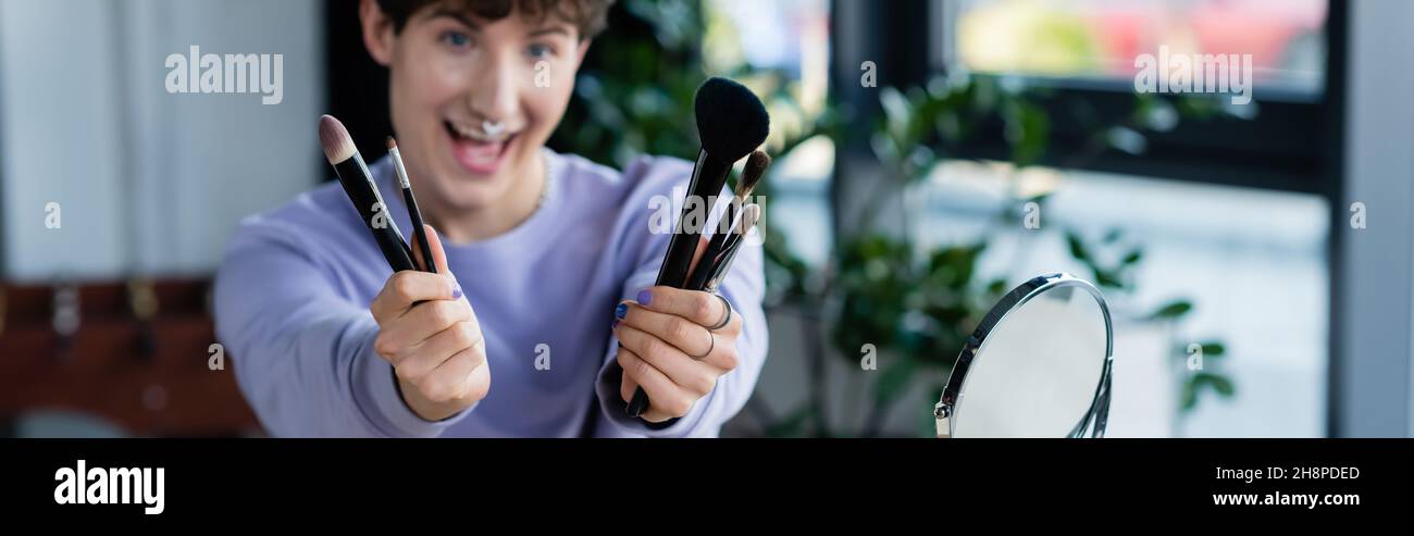 Verschwommener transgender Make-up Künstler hält kosmetische Pinsel in der Nähe von Spiegel, Banner, Stock Bild Stockfoto