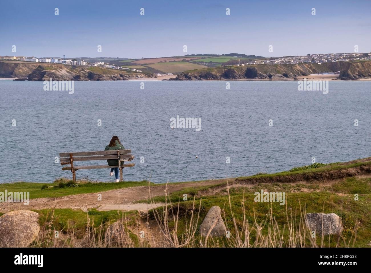 Eine Frau, die allein auf einer Bank mit Blick auf Newquay Bay in Cornwall sitzt. Stockfoto