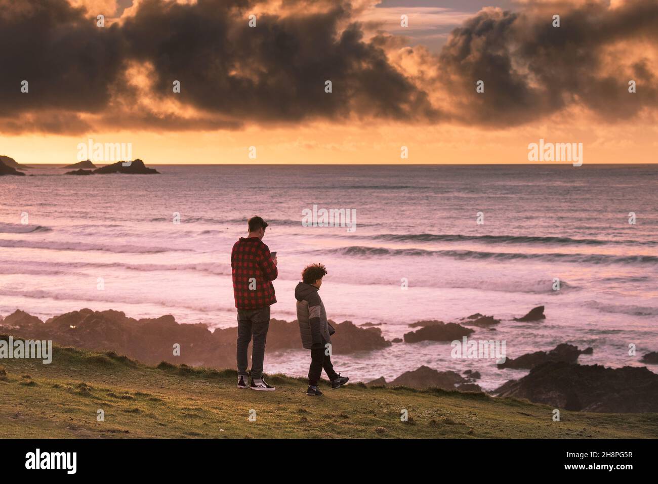 Ein erwachsener Mann und ein jüngerer Junge stehen auf der Landzunge bei Sonnenuntergang in Newquay in Cornwall. Stockfoto