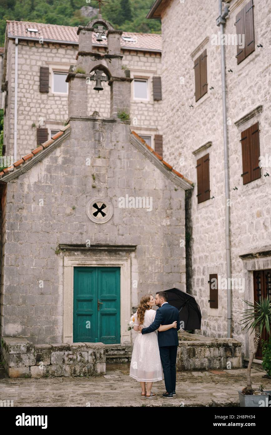 Der Bräutigam umarmt die Braut in der Nähe der grünen Tür der alten Kirche. Rückansicht Stockfoto