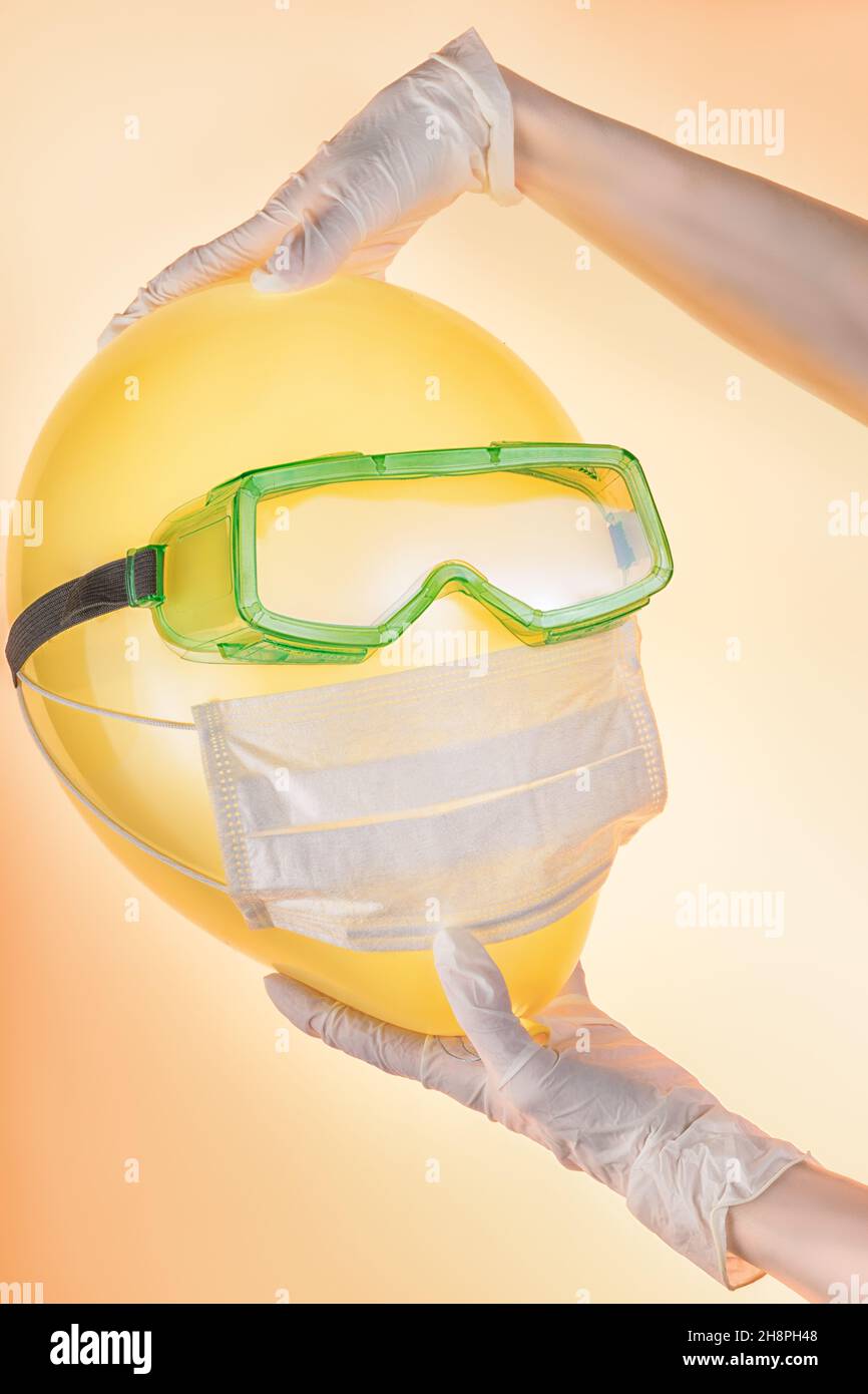 Frau Hände in Schutzhandschuhen halten Ballon in Schutzbrille und medizinische Maske. Sicherheit, Schutz während der COVID-19-Epidemie und Sperrung Stockfoto