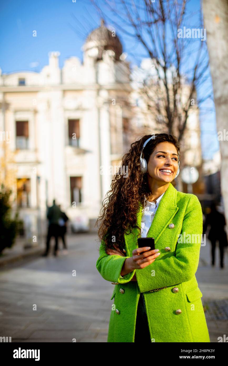 Hübsche junge Frau, die auf der Straße mit dem Smartphone Musik hört Stockfoto