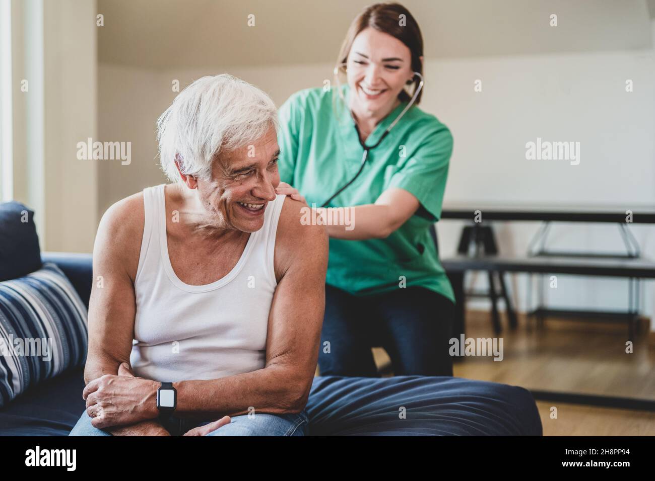 Glückliche Krankenschwester mit einem Stethoskop, das einen älteren Mann besucht, häusliche medizinische Assistentin Konzept, lächelnder Gesundheitsgast und ein älterer männlicher Patient, c Stockfoto