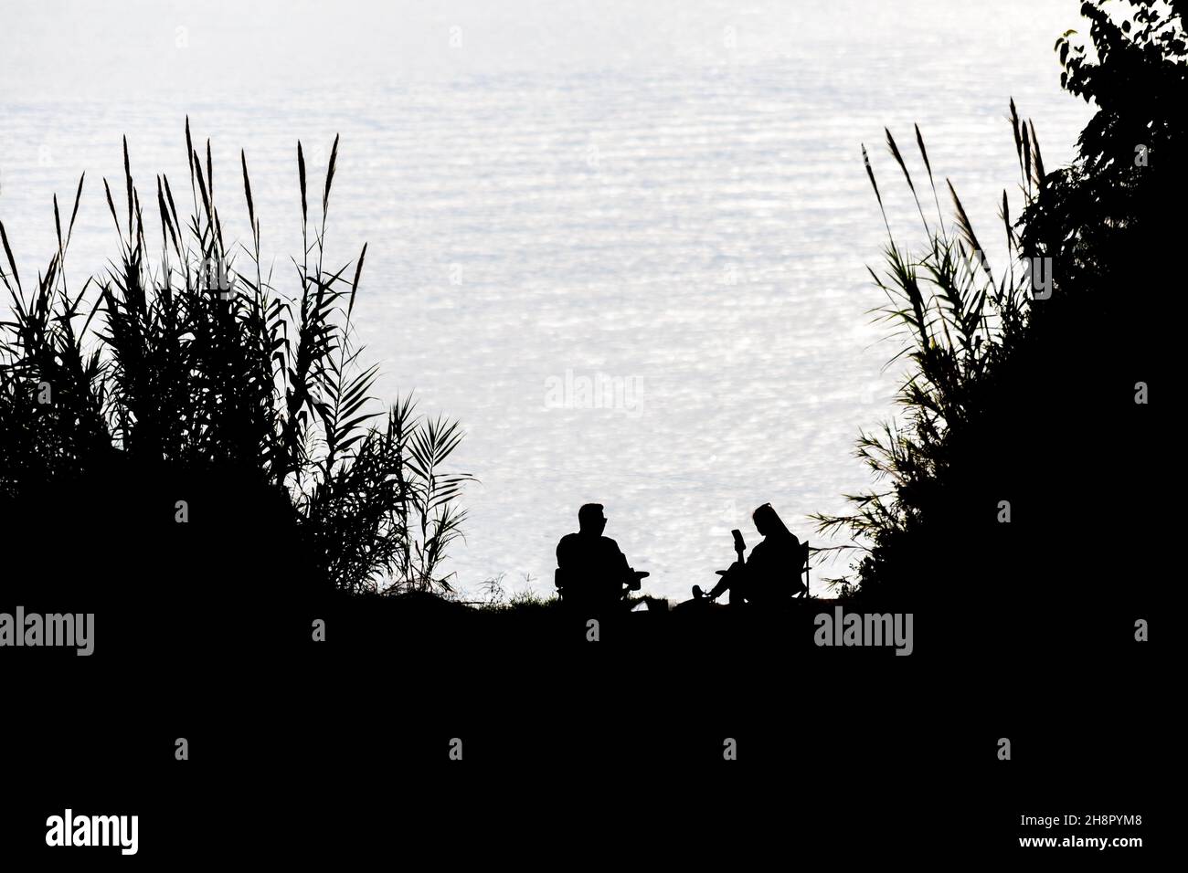 Silhouette von Ehemann und Ehefrau, die am Meer picknicken Stockfoto