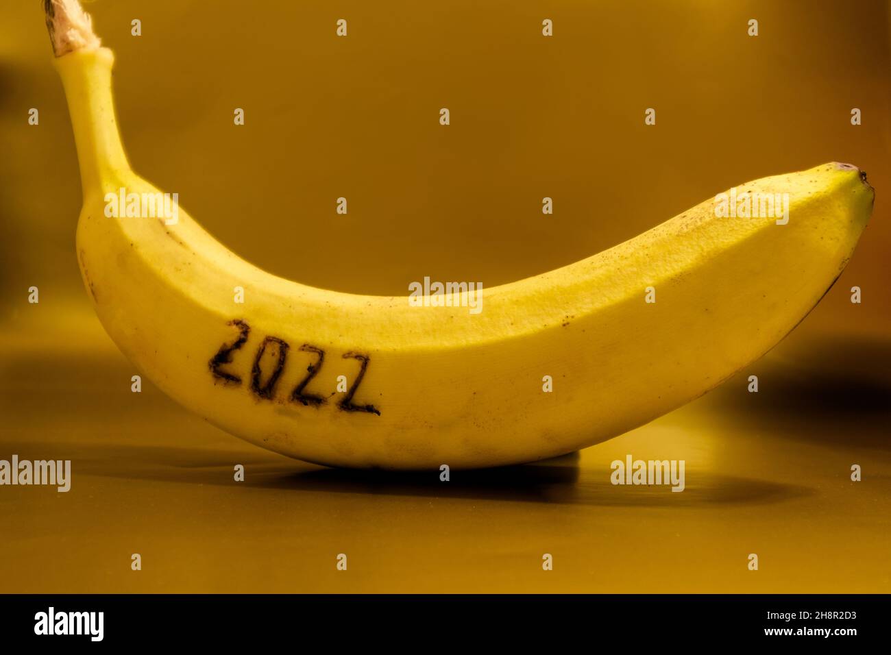 Ziffer 2022 auf einer reifen gelben Banane vor goldenem Hintergrund. Stockfoto