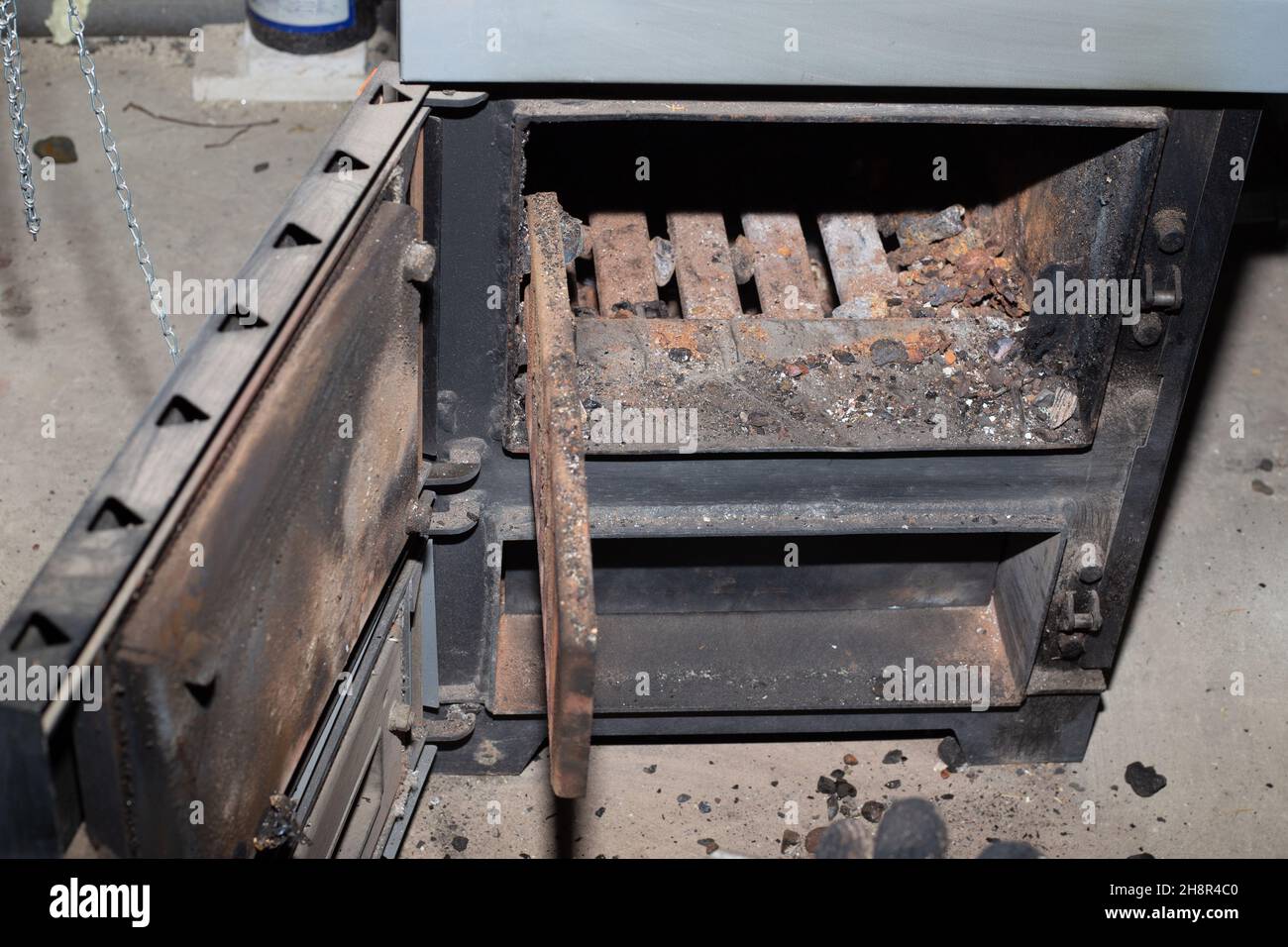 Reinigung des Festbrennstoffkessels von den Resten von Brennholz und Kohle. Kessel mit offenem Dämpfer. Heizungseffizienz im Haus. Stockfoto