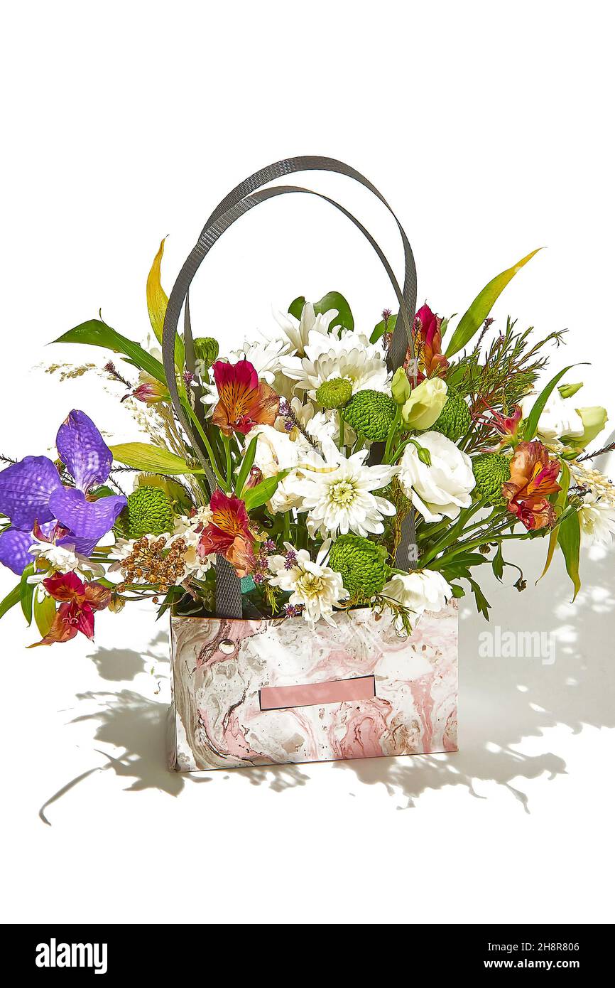 Blumenarrangement in einer Papptasche mit Kunststoffgriffen für Blumenarrangements auf weißem Hintergrund mit einem Schatten auf der rechten Seite Stockfotografie