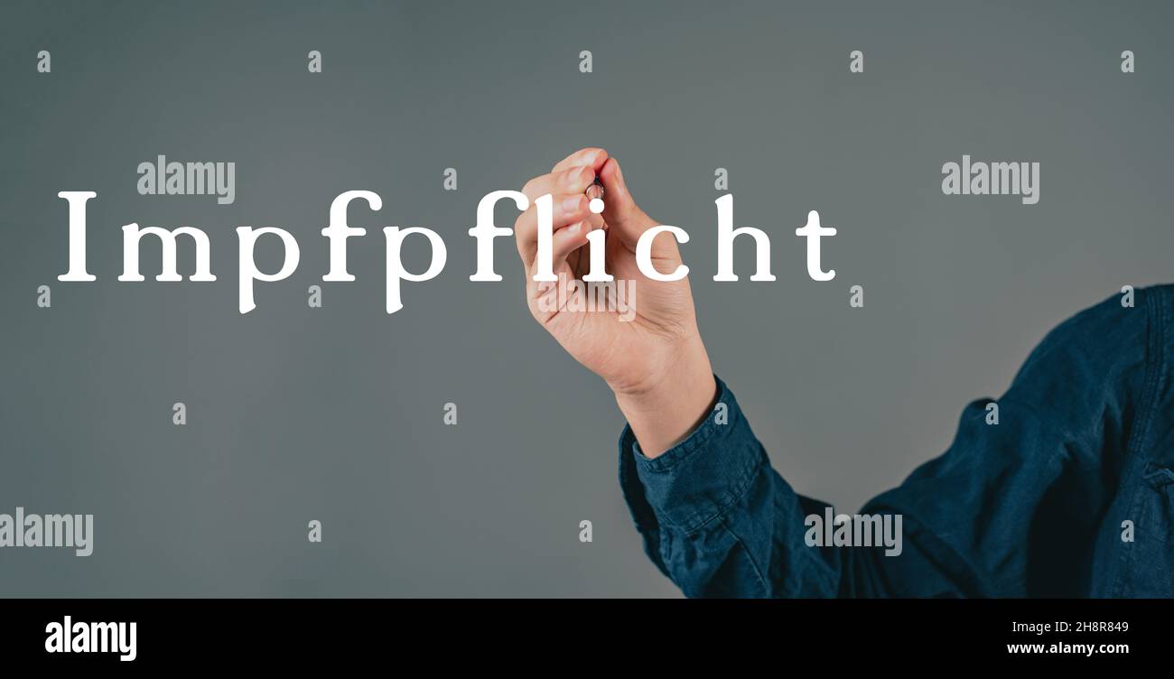 Die obligatorische Impfung steht in deutscher Sprache auf grauem Hintergrund, die Hand mit einem Stift schreibt die Botschaft Stockfoto