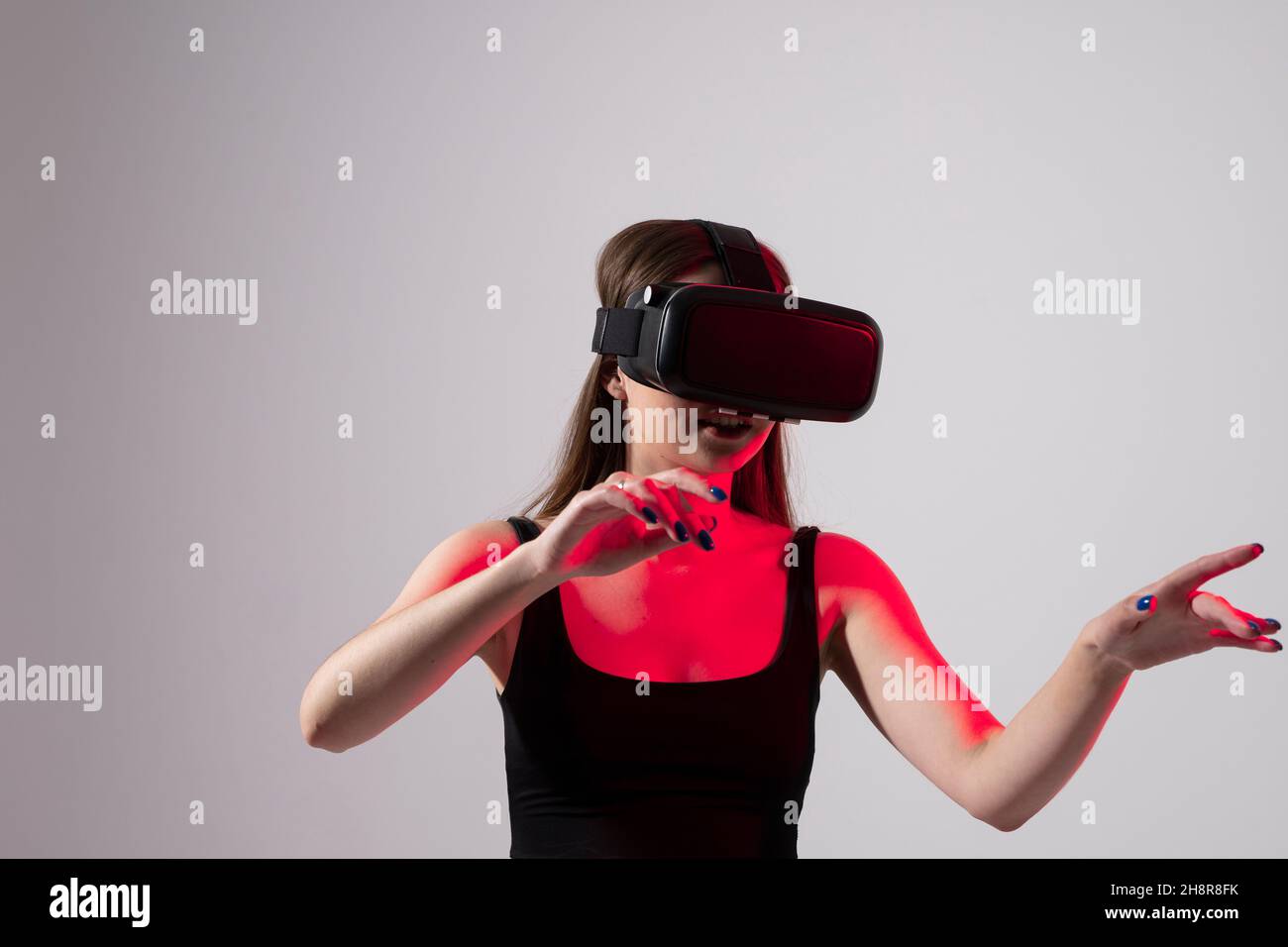 Lächeln glücklich Frau bekommen Erfahrung mit VR-Headset Brille der virtuellen Realität im Studio viel gestikulierende Hände. Technologiekonzept der Zukunft. Stockfoto