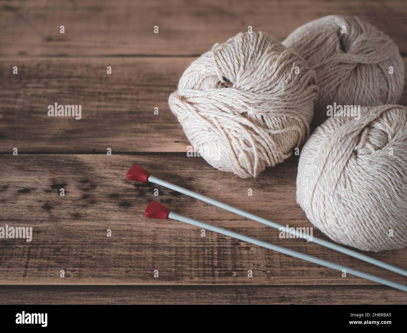 Garn und Nadeln zum Stricken, Nahaufnahme. Fadenkugeln und Stricknadeln auf Holzhintergrund Stockfoto