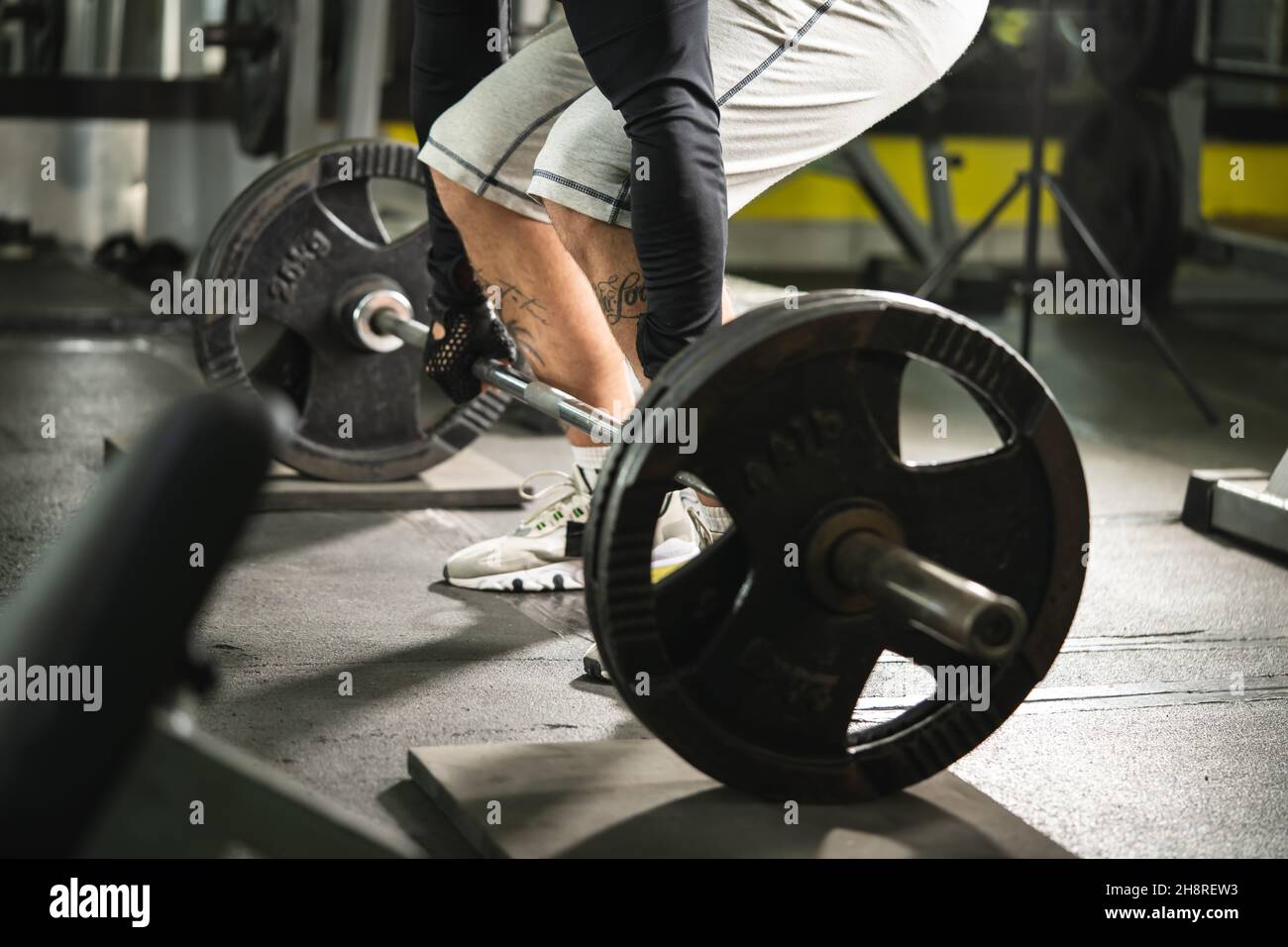 Seitenansicht eines unbekannten kaukasischen Mannes, der Hantelgewichtsgriff an Gewichten im Fitnessstudio hält, wenn er in der Totzugposition im Mittelteil des Fitnessraums den Kopierraum trainiert Stockfoto