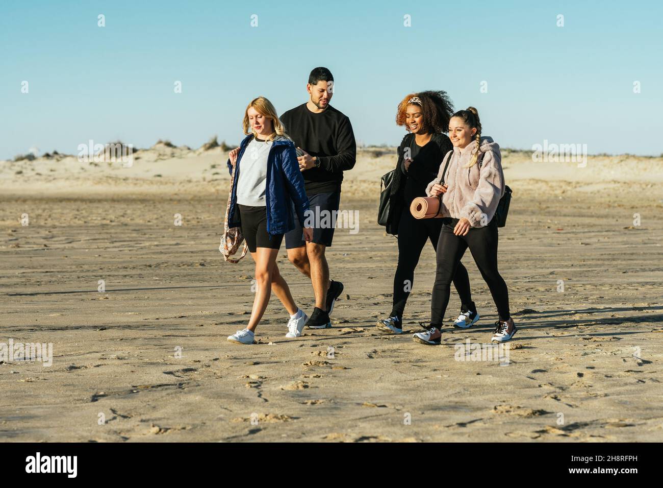 Yogalehrer und drei multiethnische Menschen, die am Strand spazieren Stockfoto
