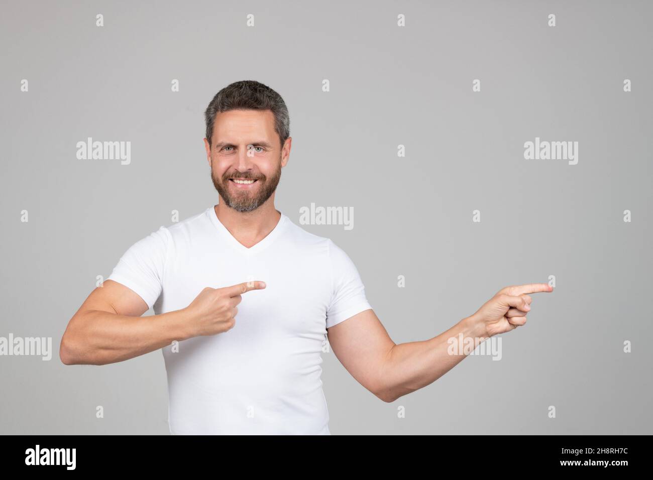 Glücklicher gutaussehender Kerl in weißem T-Shirt Lächeln zeigt Finger beiseite Werbegeste, Werbung Stockfoto