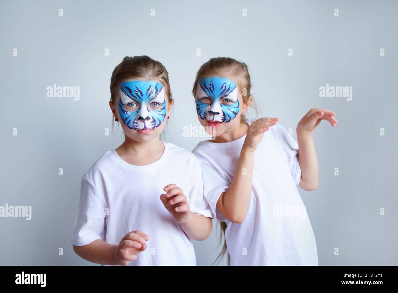 Zwei Schwesternmädchen mit Aqua-Make-up in Form eines blauen WasserTierkreiszeichens zeigen einen Tiger auf weißem Hintergrund, ein konzeptionelles Symbol des neuen 2022 Stockfoto