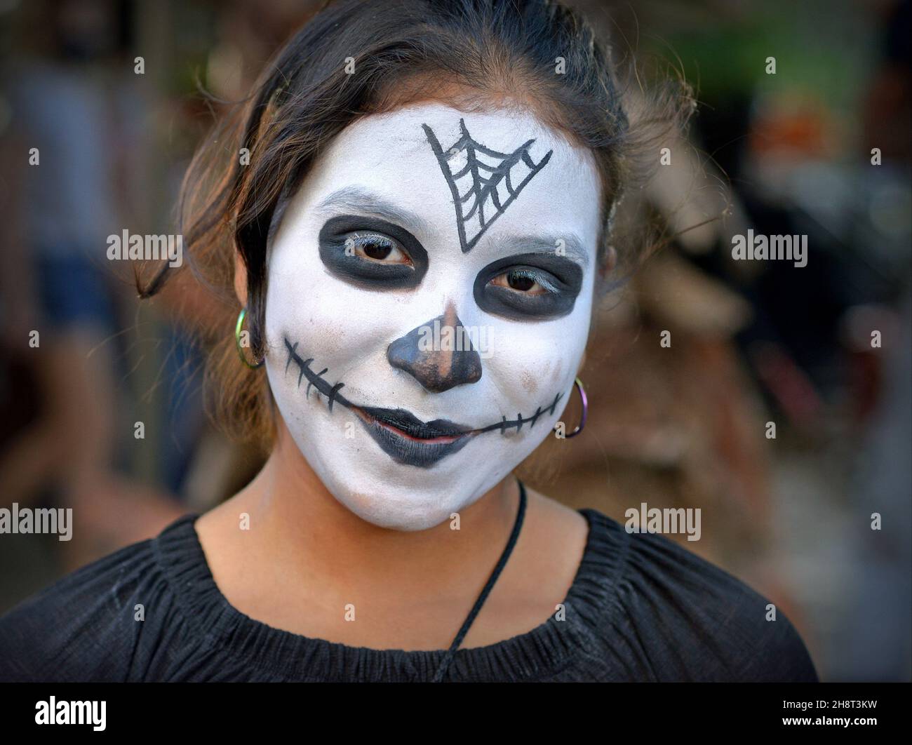 Junge Mexikanerin mit traditionellem weißen Catrina Face Make-up und schwarzen Augen am Tag der Toten (Día de los Muertos) schaut auf den Zuschauer. Stockfoto