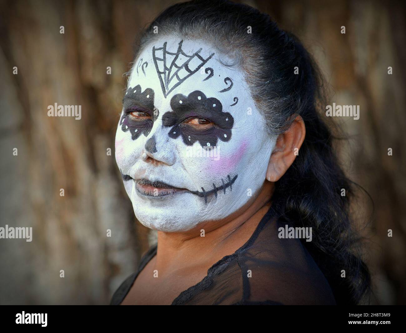 Reife Mexikanerin mit traditionellem weiß gestrichenen Catrina Face Make-up und schwarzen Augen am Tag der Toten (Día de los Muertos) schaut auf den Betrachter. Stockfoto