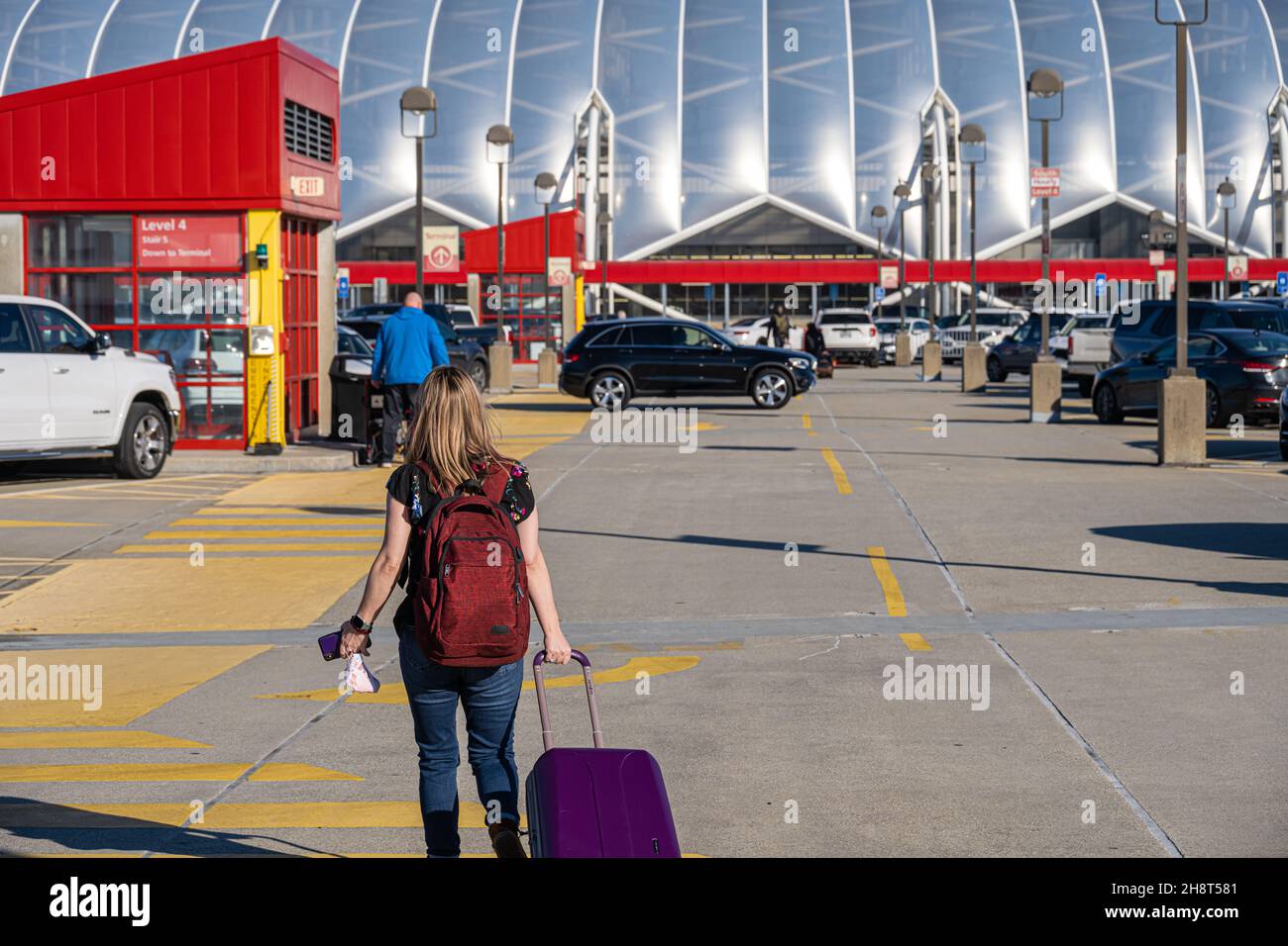 Weibliche Reisende, die einen Rucksack trägt und einen Koffer auf dem oberen Parkdeck des Hartsfield-Jackson Atlanta International Airport in Atlanta, GA, zieht. Stockfoto