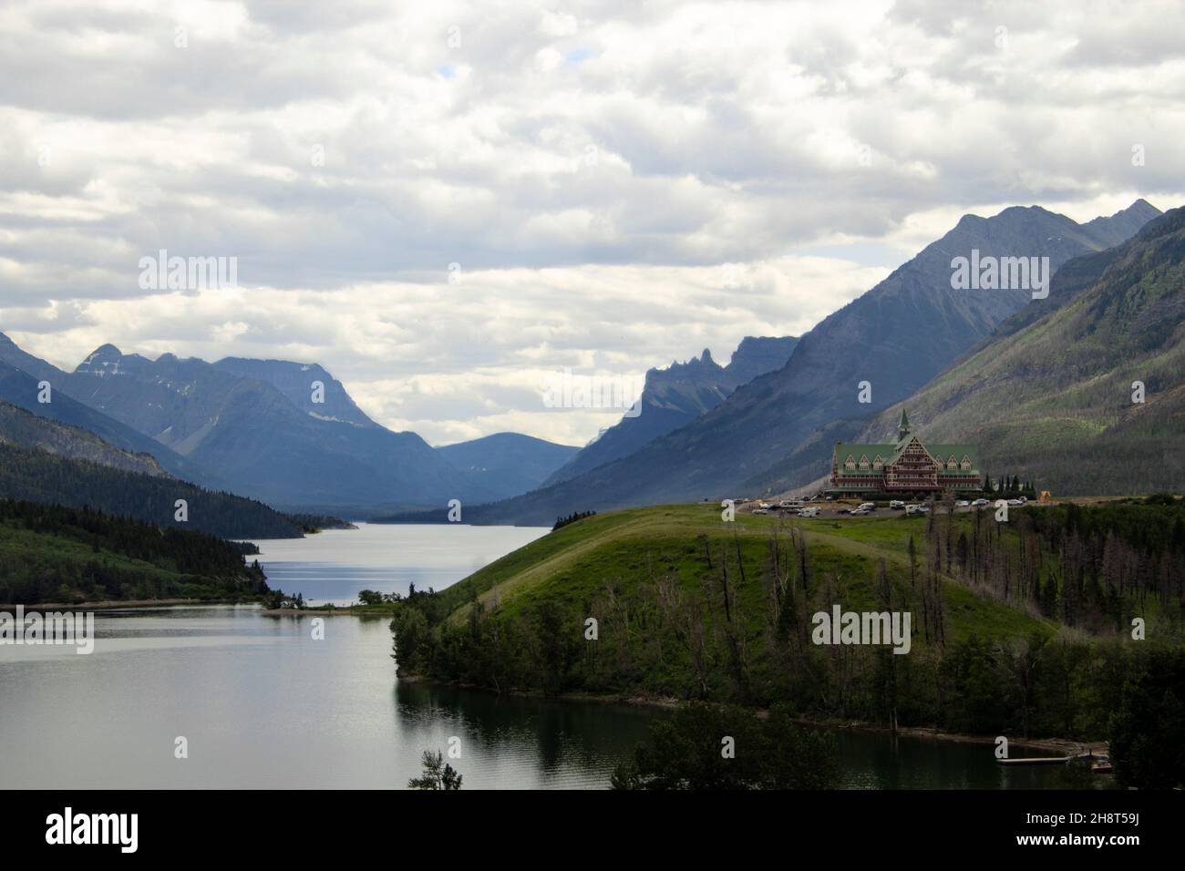 Prince of Wales Hotel am Ufer des Waterton Lake mit grünen Hügeln und Bergen im Hintergrund Stockfoto