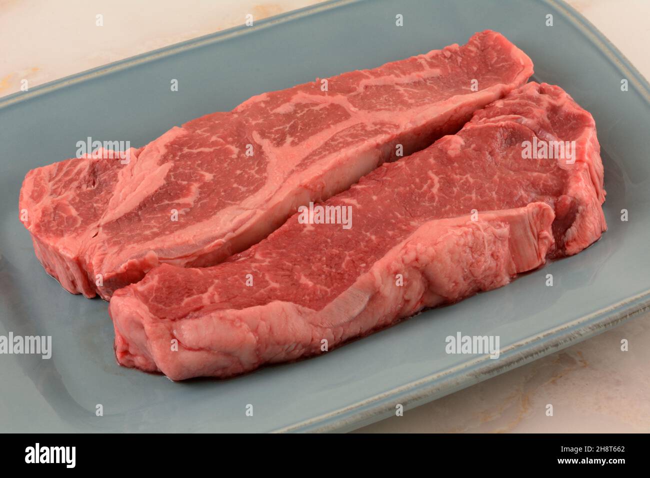Zwei rohe New Yorker Steaks, die auf einem blauen Servierteller gegrillt werden können Stockfoto
