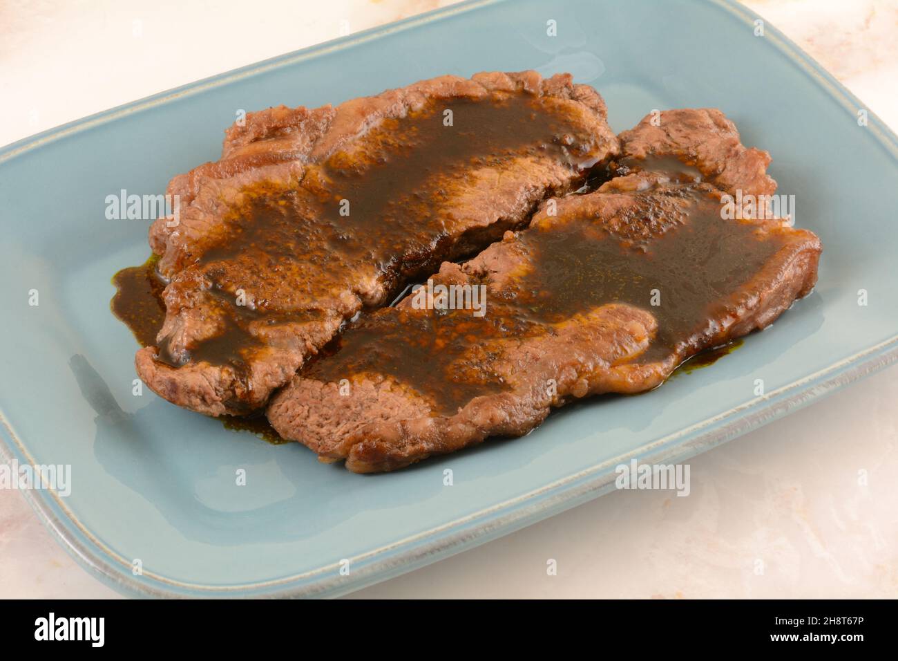 New York Streifensteak mit Knoblauchsauce auf blauem Servierteller Stockfoto