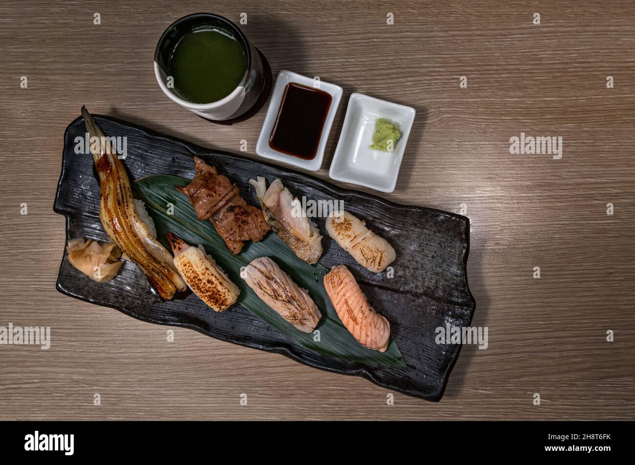 Draufsicht Bild von gegrilltem Sushi auf schwarzem Teller mit grünem Tee Tasse, gegrillte Vielfalt an gesunden Sushi, Lachs, Thunfisch, Garnelen, Rindfleisch und Engawa. Stockfoto