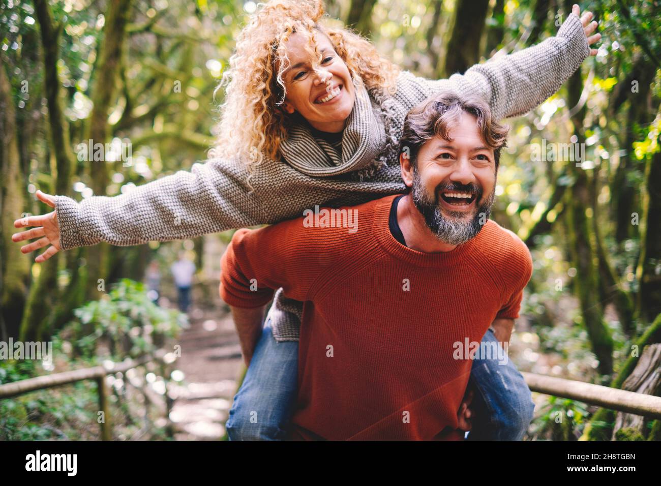 Überglücklich Erwachsene Paare haben Spaß zusammen im Outdoor-Park in Freizeitaktivitäten. Mann trägt Frau im Huckepack und lacht viel. Liebe und Leben reifen pe Stockfoto