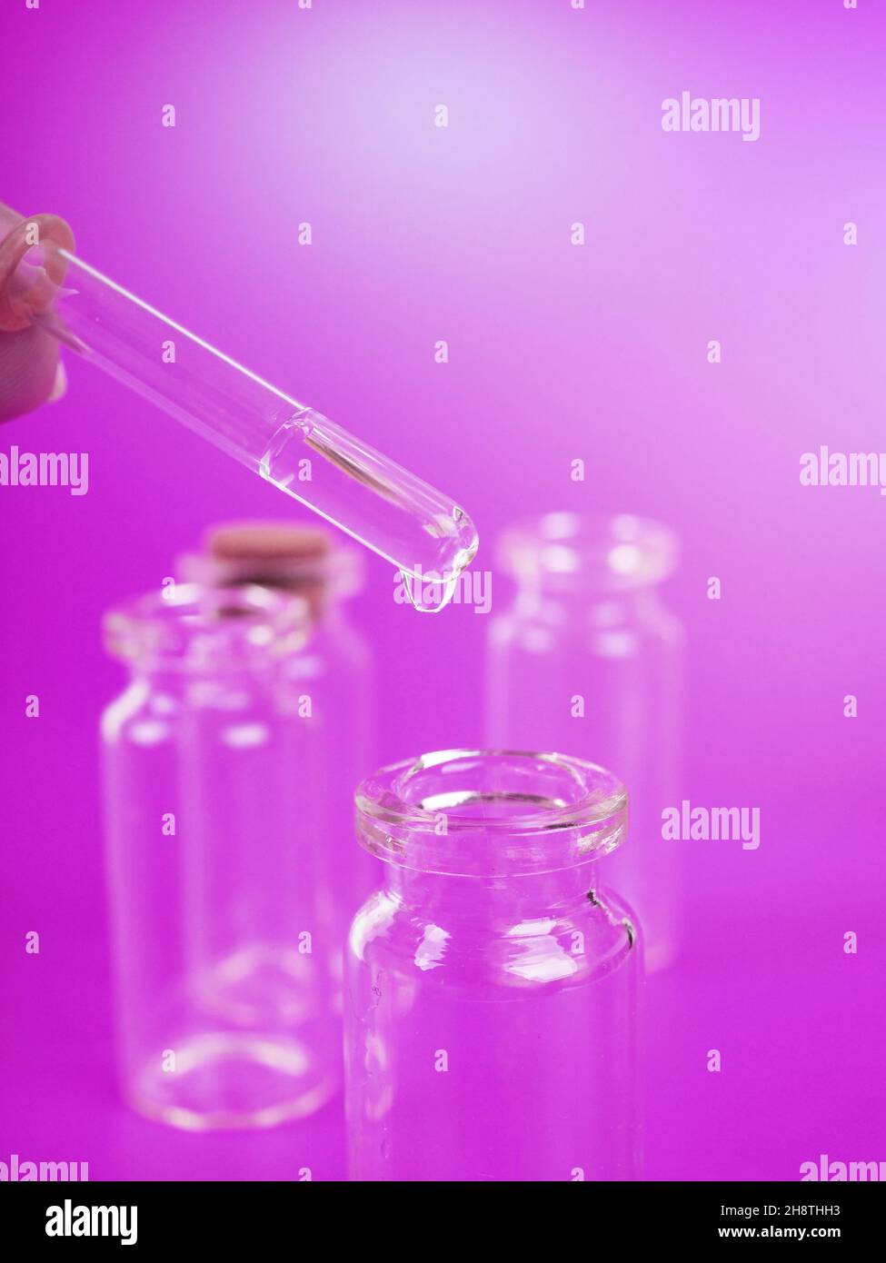 Tropfen Flüssigkeit aus einer Pipette in eine medizinische Flasche, Forschungskonzept, neue Medikamente und Wissenschaft, auf einem hellen rosa, blauen und violetten Hintergrund. Stockfoto