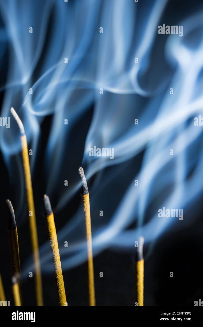 Blauer Rauch von Räucherstäbchen vor schwarzem Hintergrund Stockfoto