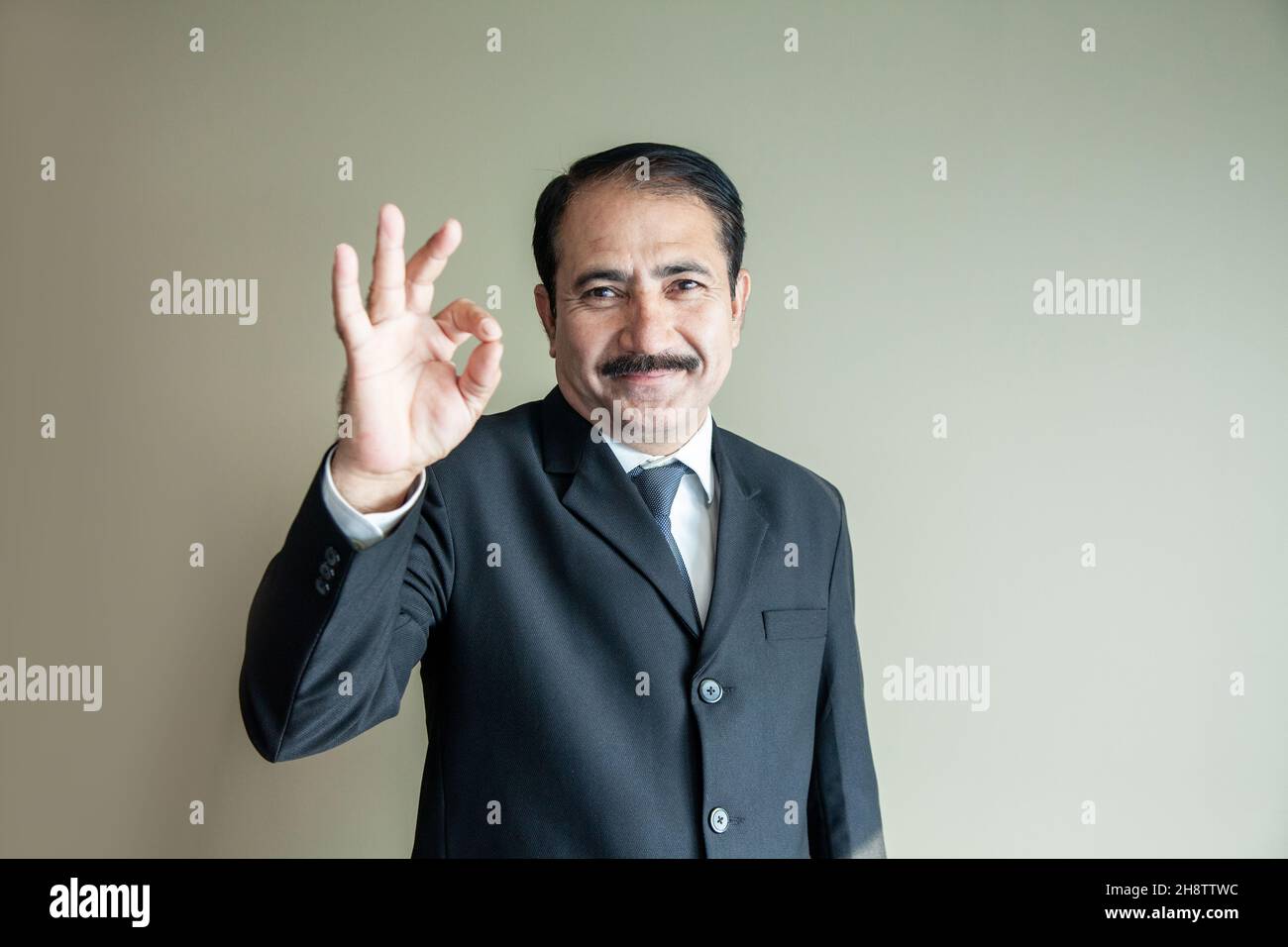 Intelligenter reifer älterer Geschäftsmann mit Schnurrbart, der ein OK-Zeichen mit seinem handtragenden Anzug und Krawatte zeigt Stockfoto