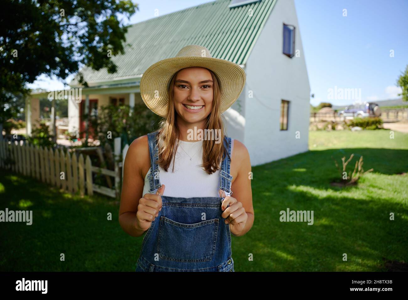 Lächelnde kaukasische Farmerin, die im Freien mit Latzhose steht Stockfoto