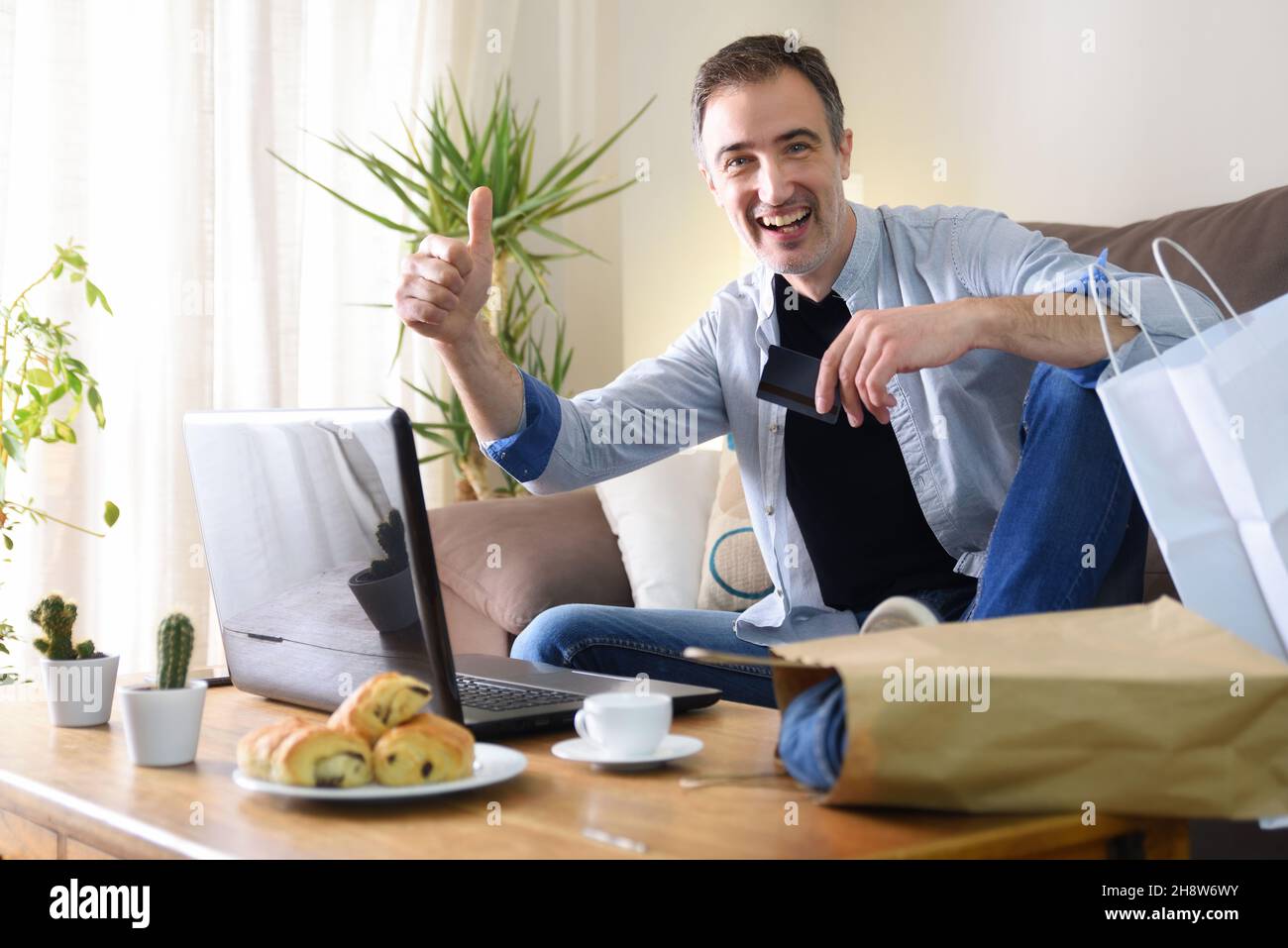 Ein fröhlicher Mann, der von einem Laptop aus zu Hause auf dem Sofa online einkaufen geht und ein Schild sieht, das in Ordnung ist. Horizontale Zusammensetzung. Stockfoto