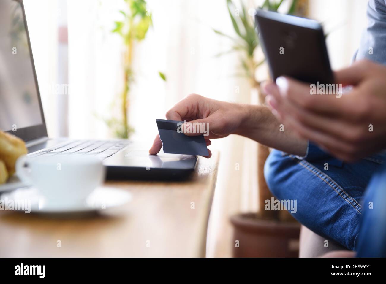 Online-Bezahlkonzept auf dem Laptop mit Handy und Kreditkarte mit Mann zu Hause sitzen. Horizontale Zusammensetzung. Stockfoto