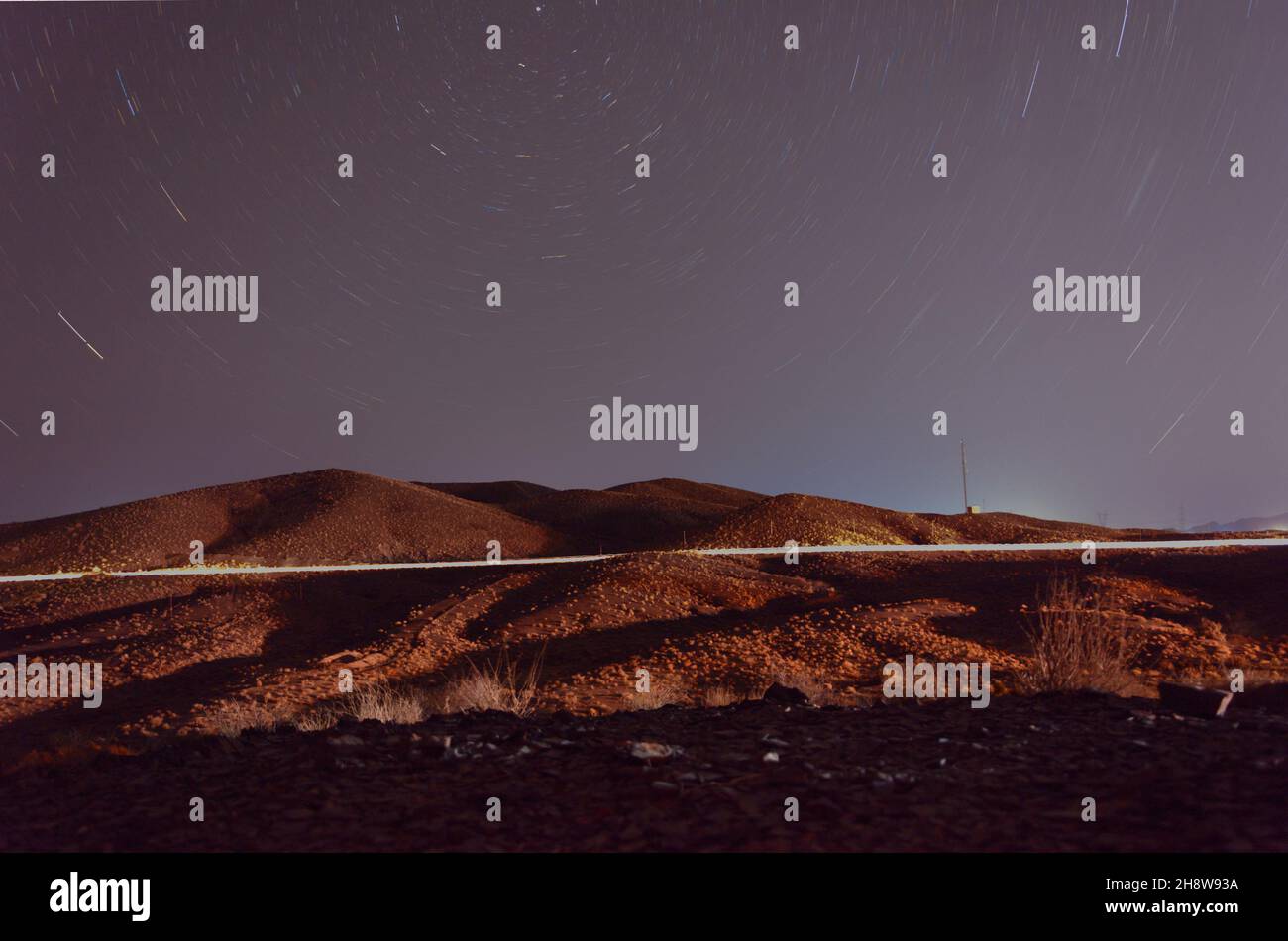 Nachtansicht von Pflanzen und Hügeln in der Wüste mit Licht- und Sternspuren und Nordstern am Rahmen im iran Stockfoto