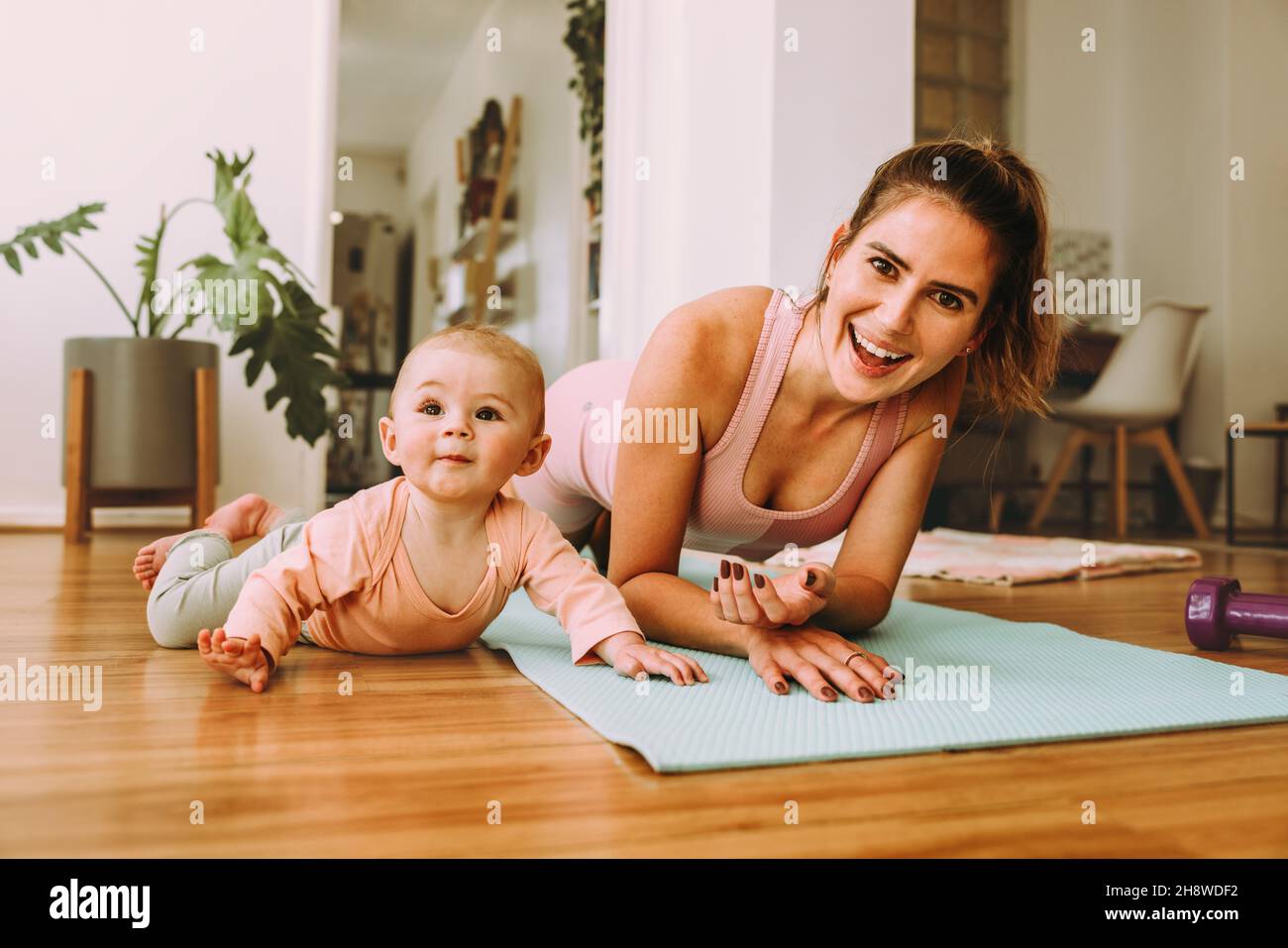 Fröhliche Mutter macht Planübungen mit ihrem Baby zu Hause. Glückliche junge Mutter, die mit ihrem Baby auf einer Übungsmatte trainiert. Neue Mutter Bonding mit ihrem Baby d Stockfoto