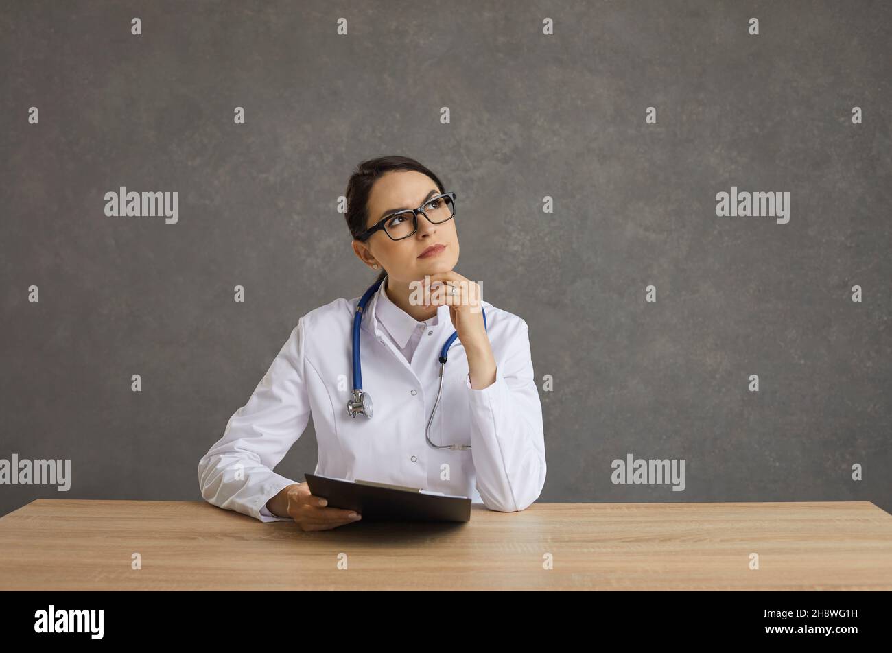 Porträt einer ernsthaften Ärztin, die mit einem nachdenklichen Gesichtsausdruck an einem Tisch sitzt. Stockfoto
