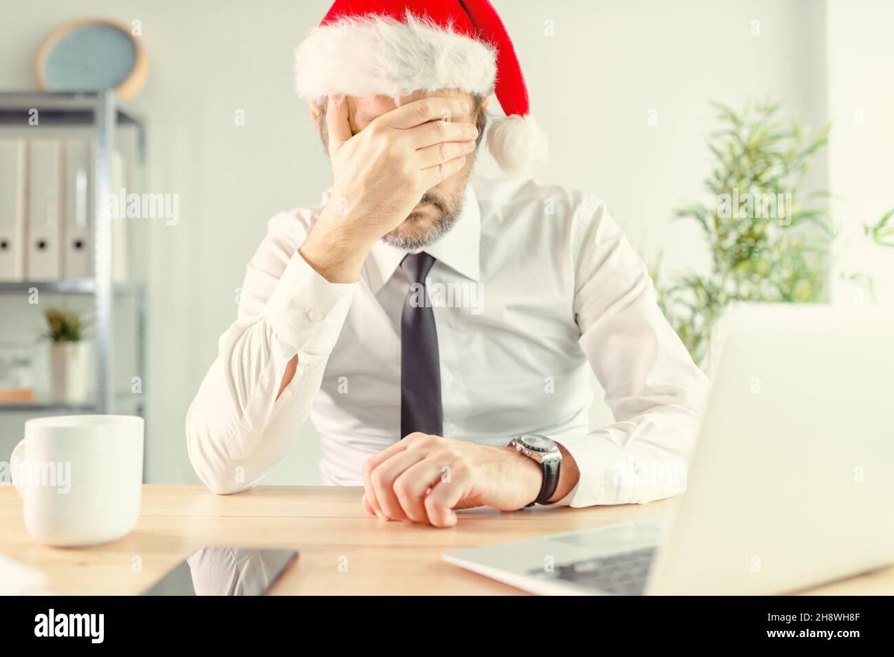 Neujahrsdepression, Geschäftsmann im Büro trägt Weihnachtsmann Hut Gefühl einsam und deprimiert mit Hand bedeckendes Gesicht, selektive Konzentration Stockfoto