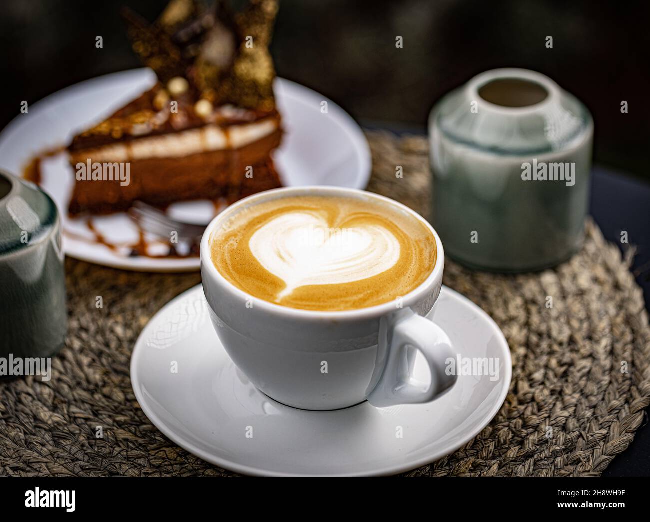Coffee Latte Art in weißer Tasse mit einem Stück Schokoladenkuchen auf dem Hintergrund Stockfoto