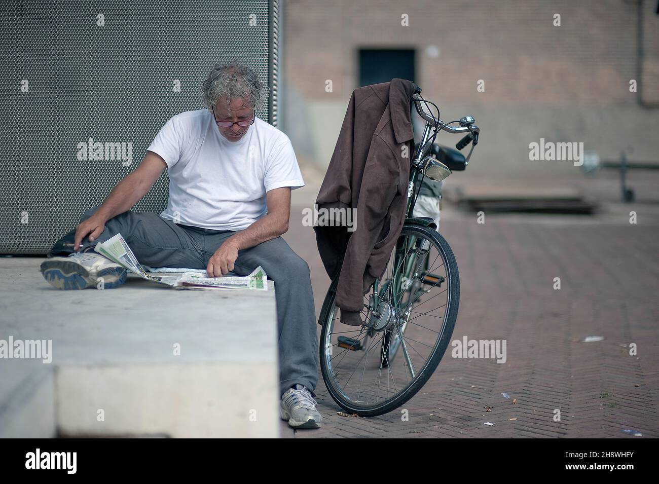 Rotterdam, Niederlande. Ein erwachsener Mann liest seine Zeitung, während er während einer Pause sitzt und sich entspannt, während er mit dem Fahrrad unterwegs ist. Stockfoto