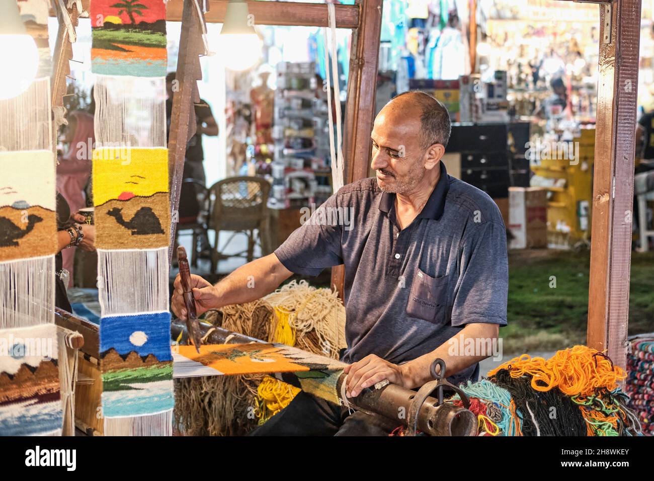 Ägyptischer Mann, der bunte kleine Teppiche als Souvenirs für Touristen auf dem Handwebstuhl auf der Nachtsstraße spinnt. Stockfoto