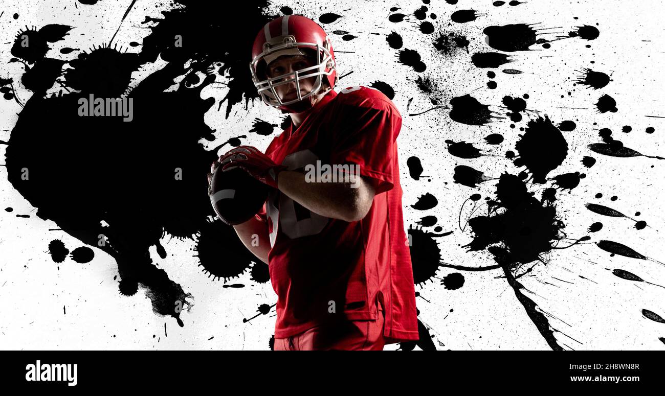 Amerikanischer Fußballspieler in roter Uniform hält den Ball vor abstrakt bespritzten Hintergrund Stockfoto