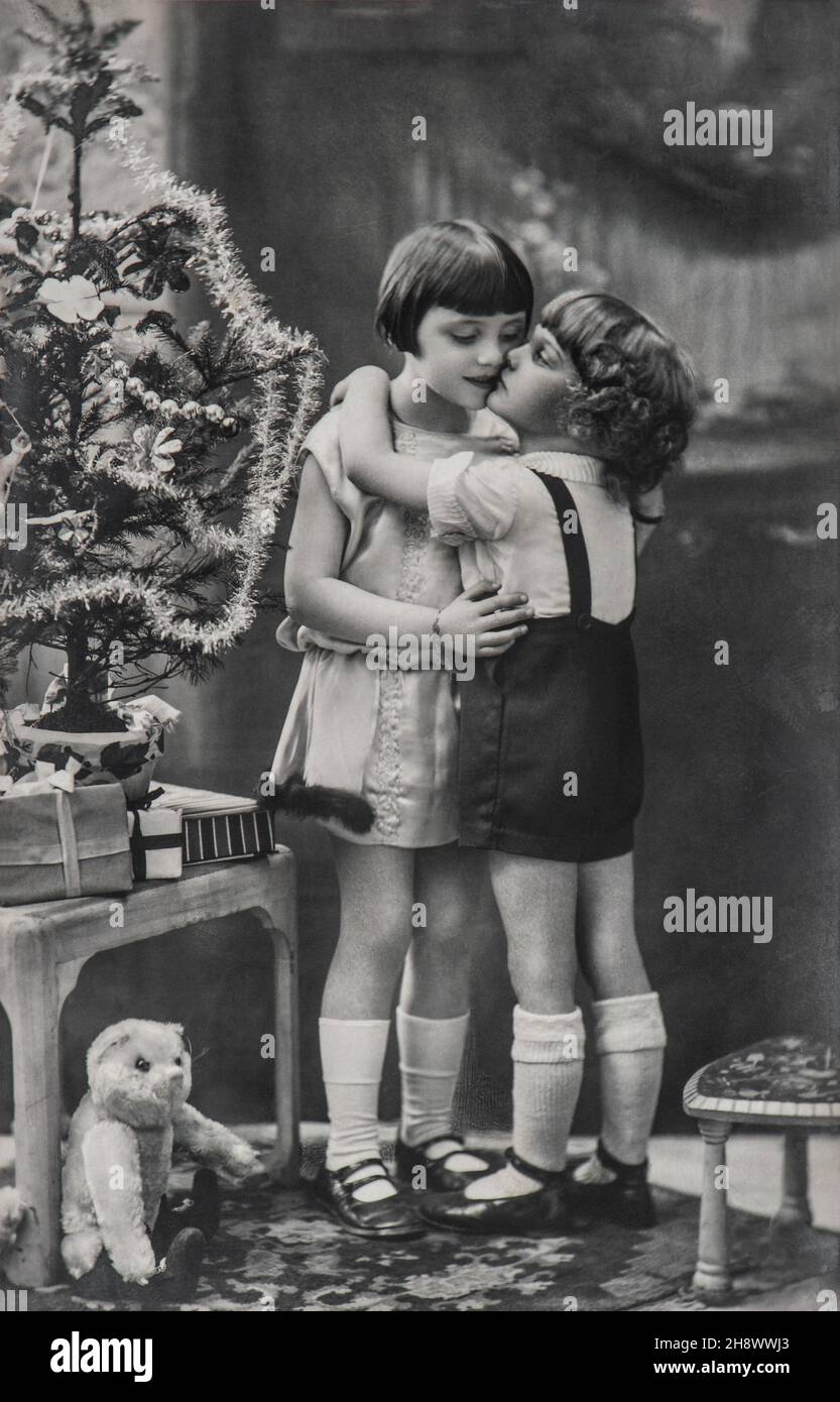 Niedliche Kinder mit Weihnachtsbaum, Geschenke und Vintage-Spielzeug. Antikes Bild mit original Filmkörnung Stockfoto