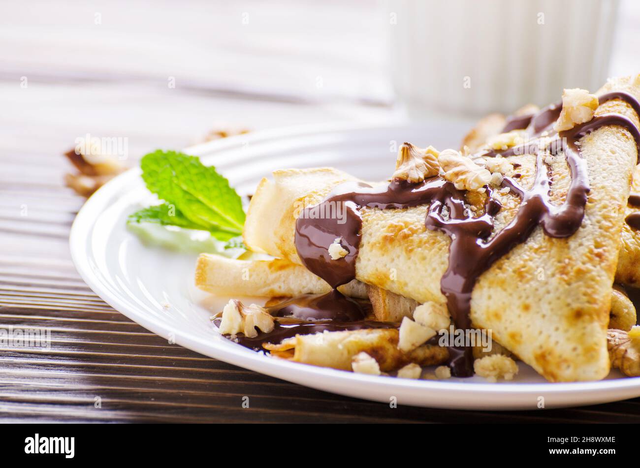 Französische Crêpes mit Schokoladensauce und Walnüsse in Keramik Teller auf hölzernen Küchentisch Stockfoto