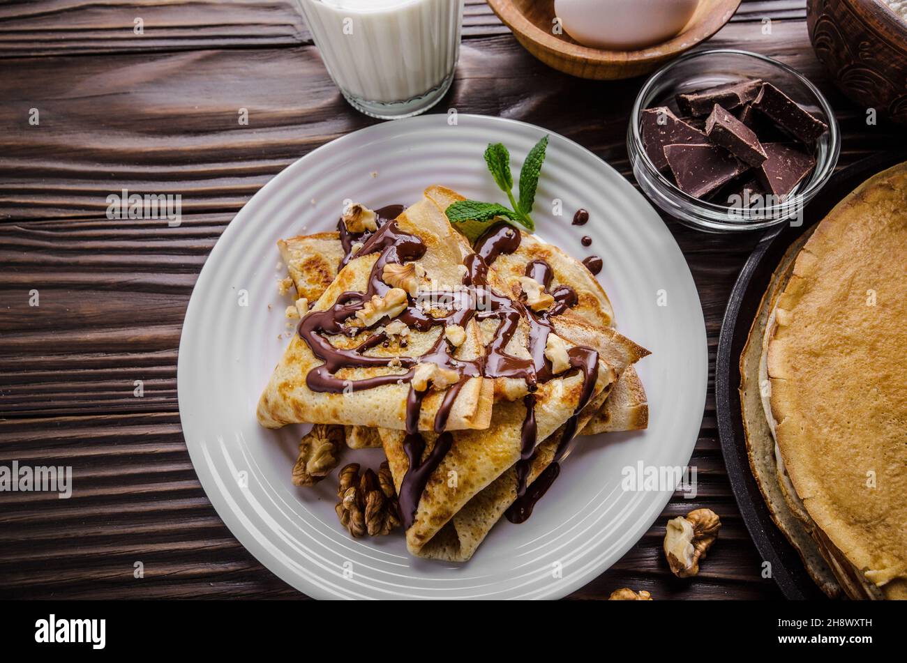 Französische Crêpes mit Schokoladensauce Walnüsse Eier und Mehl auf hölzernen Küchentisch Stockfoto