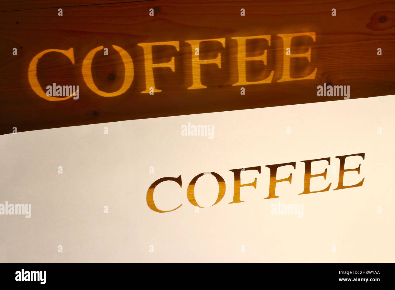 Das Wort Kaffee von Hand aus Papier geschnitten und dann projiziert auf eine hölzerne Oberfläche mit künstlichem Licht Stockfoto