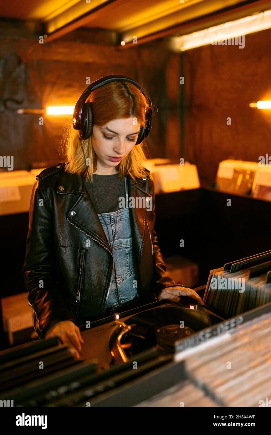 Frau in Lederjacke hört Lied über Vintage-Plattenspieler mit Vinyl-Disc, während sie im Laden steht Stockfoto