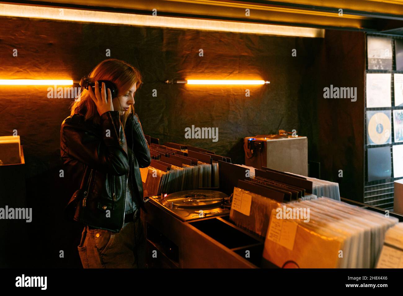 Frau in Lederjacke hört Lied über Vintage-Plattenspieler mit Vinyl-Disc, während sie im Laden steht Stockfoto